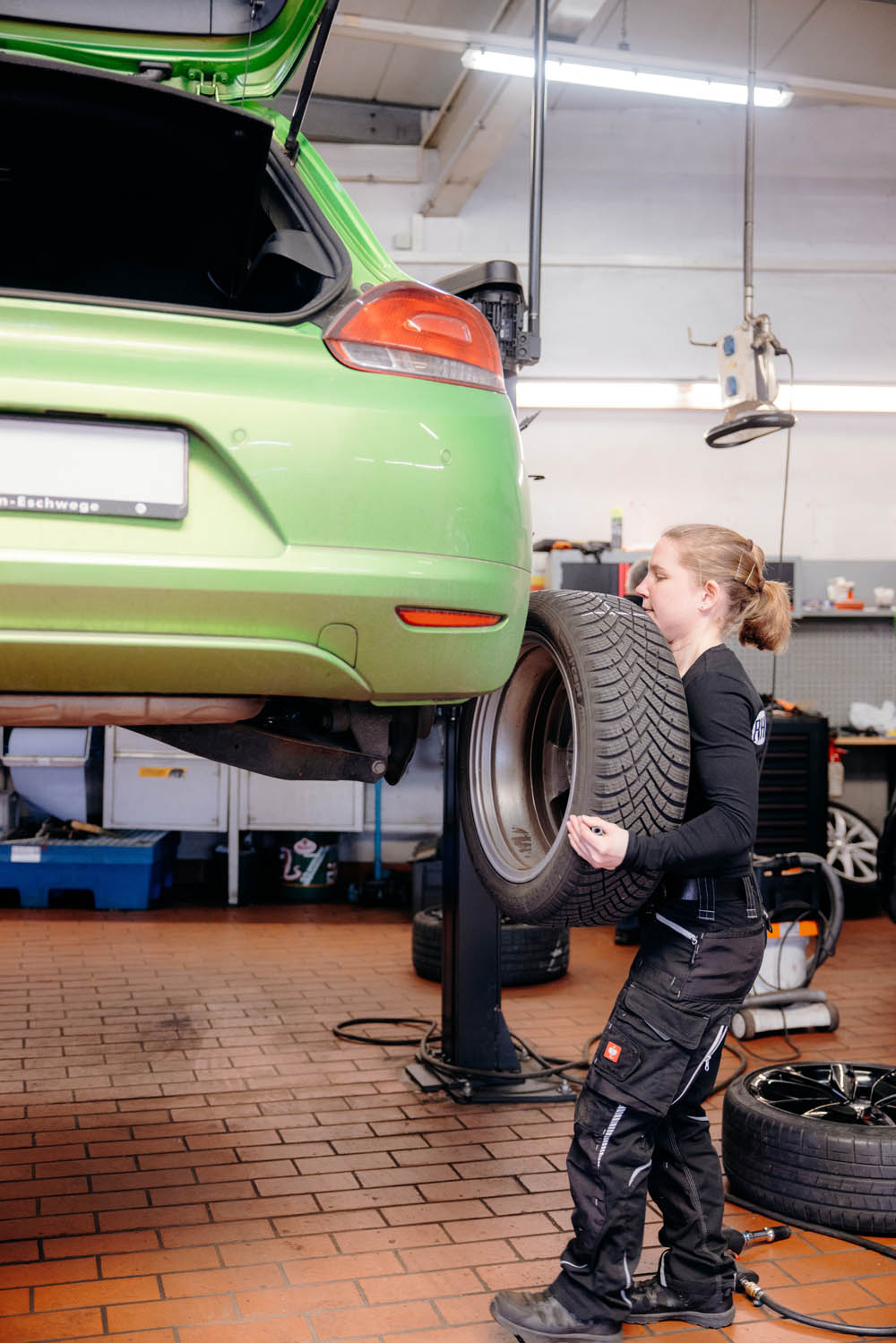 Fachgerechter Reifenwechsel direkt in unserer Werkstatt Mechanikerin wechselt Reifen an aufgebocktem Fahrzeug